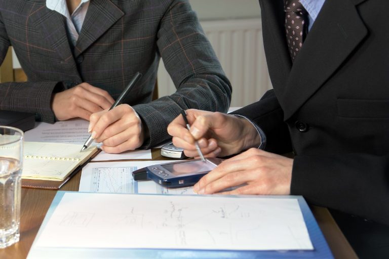 Zwei Menschen sitzen sich am Tisch gegenüber und berechnen zusammen etwas.